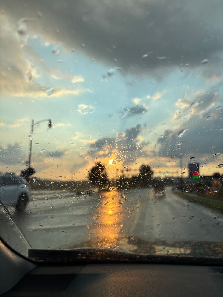 Sunshine with few clouds as it rains on a car windshield 