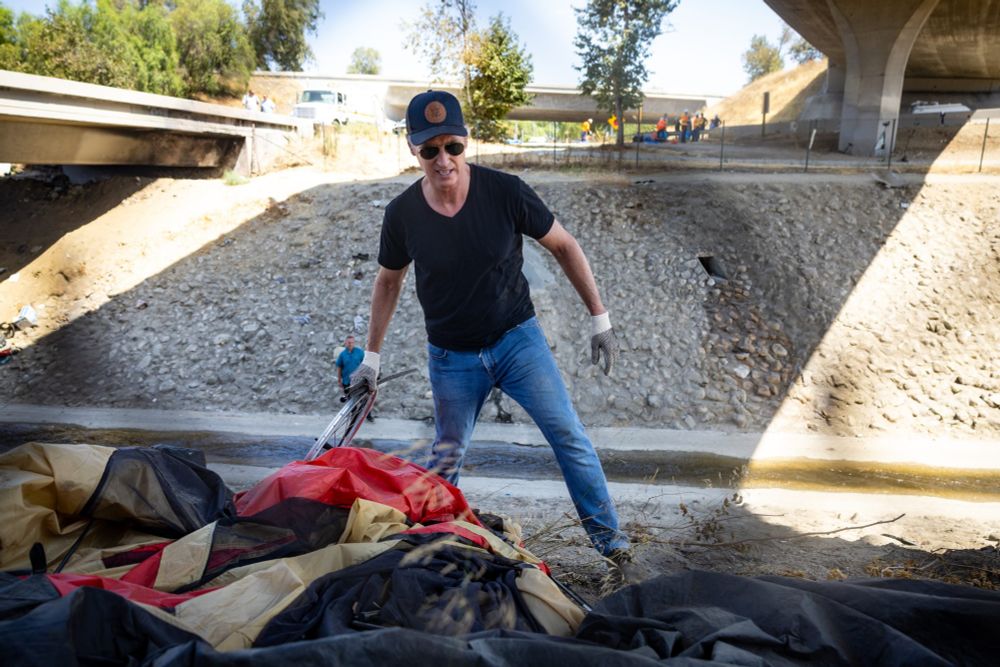 Photo of Gavin Newsom throwing away the belongings of people living on the street.