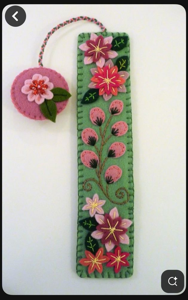 Felt bookmark with a green base, several pink flowers, and dark green leaves. There are embroidery detail accents, and a pink end piece. 