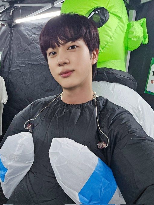 Jin of BTS in an inflatable suit that makes him look like he has been abducted by a green-faced alien