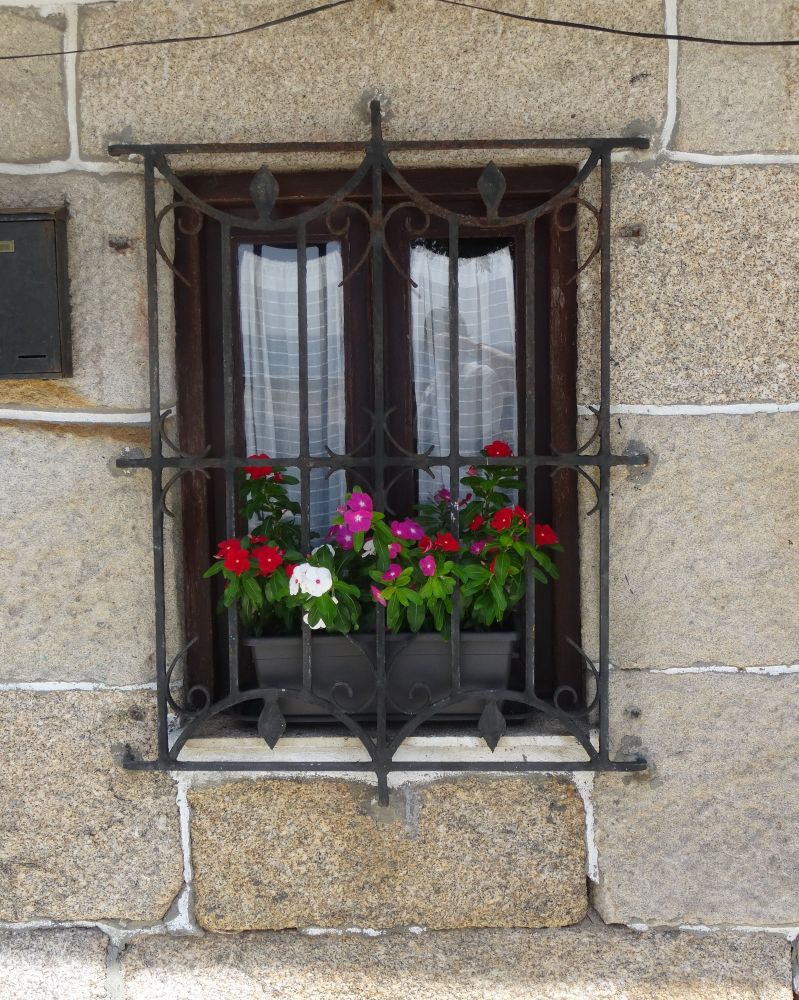 Ventana de rejas en una pared de piedras con una maceta llena de flores de colores.
