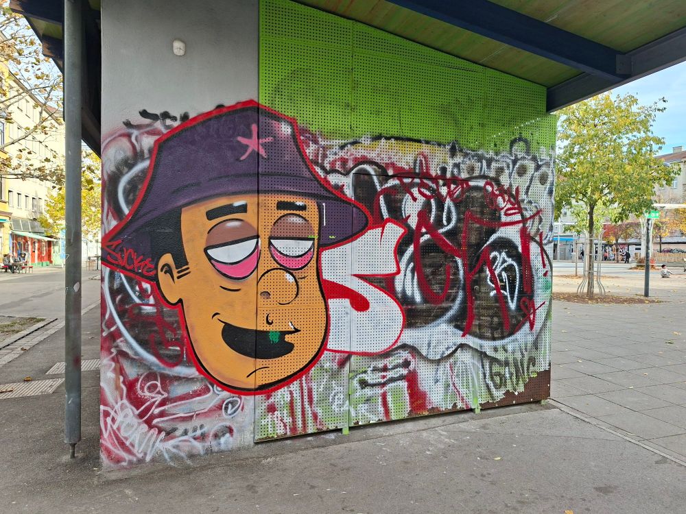 Graffiti, Kopf mit Hut über nicht leserlicher Schrift, dahinter der Yppenplatz. 