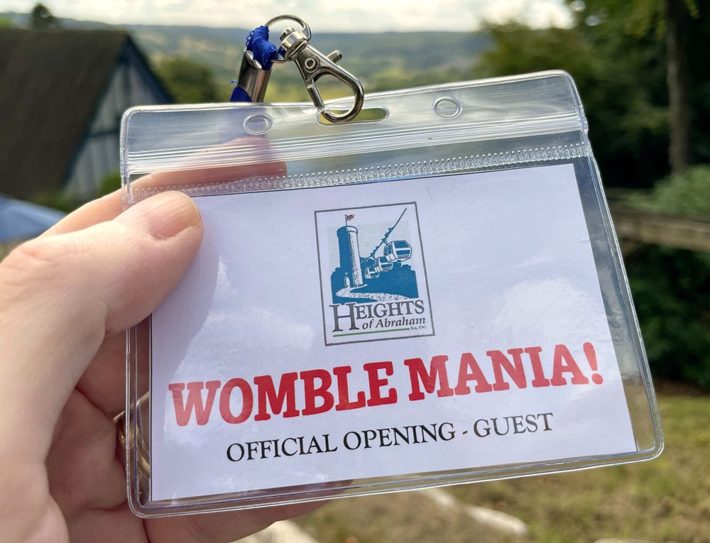 A hand holding a lanyard with a pass that says:
Heights of Abraham
Womble Mania!
Official opening - guest
In the background are the hills of the Peak District National Park.