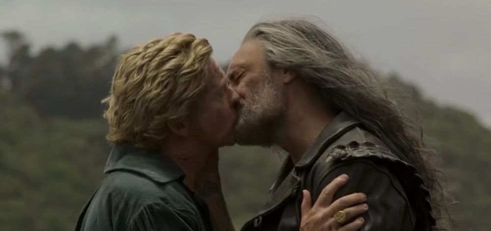 A close up frame from ofmd season 2 episode 8 of stede and ed kissing in the beach, stede is holding his arm