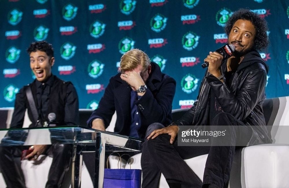 A photo from the ofmd panel at ECCC 23 of vico in izzy cosplay with an excited face, rhys covering up his and samba looking mischievous with the microphone 
