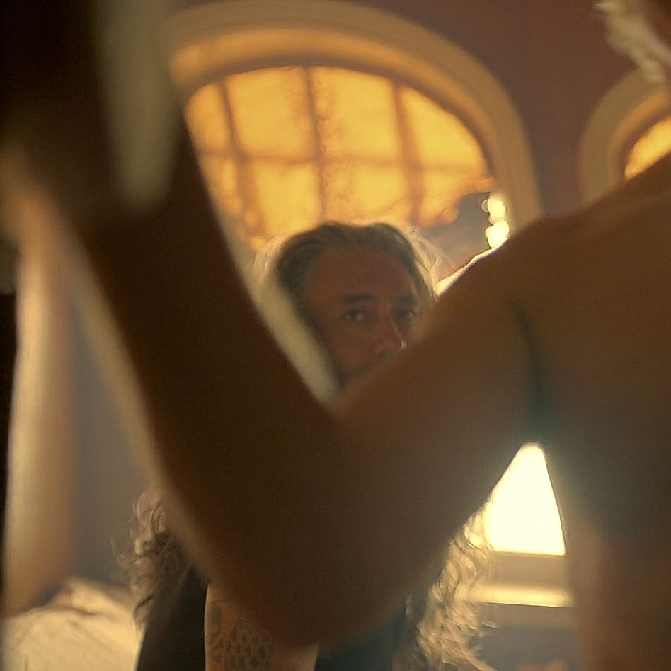 A picture from ofmd season 2 episode 6 of ed sitting on the bed nook looking at shirtless stede as he closes the curtain before they have sex