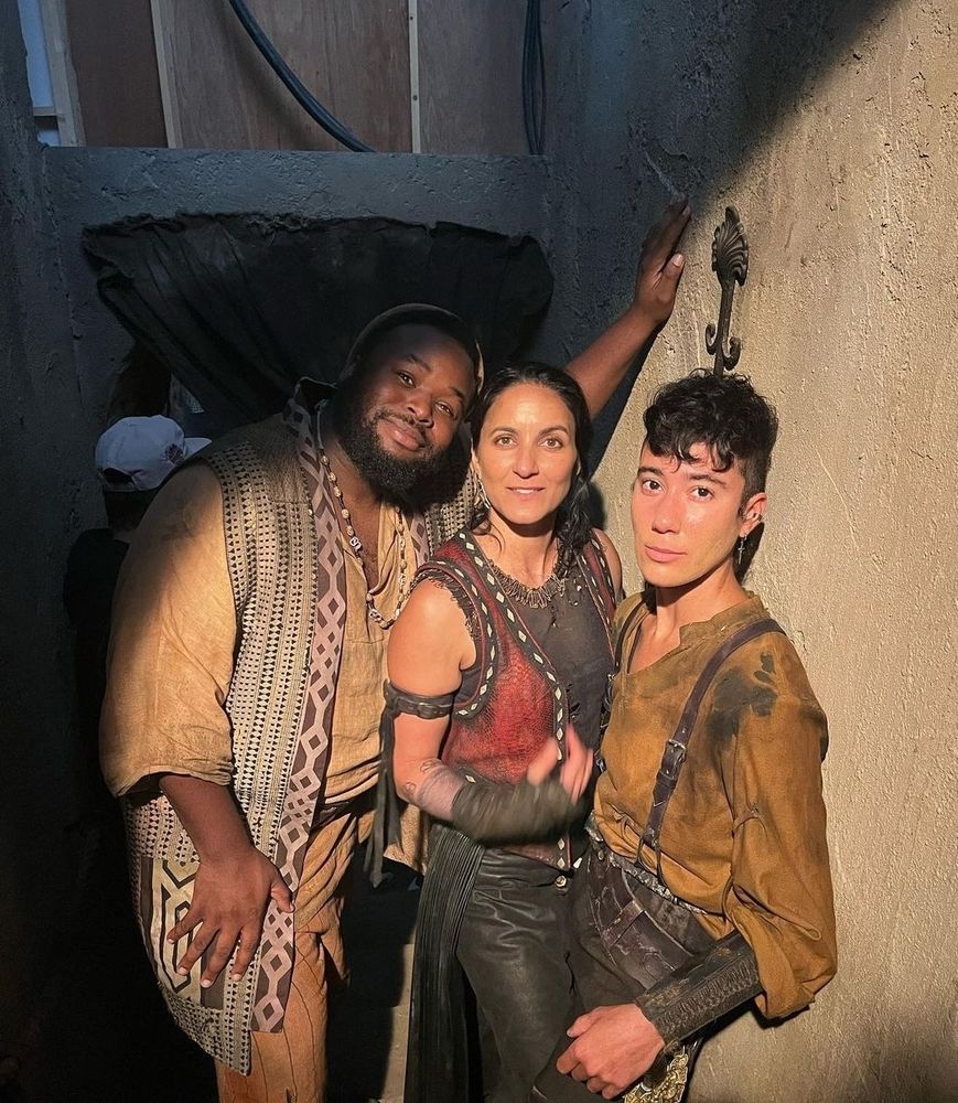 A behind the scenes picture from ofmd season 2 of samson, madeleine and vico standing close together against a wall