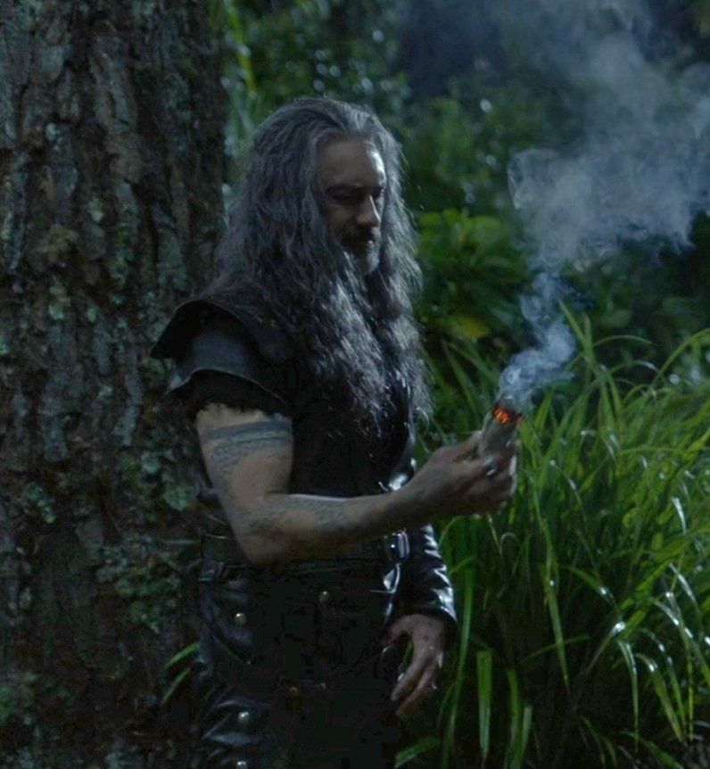 A still from ofmd season 2 episode 4 of ed standing in the woods, holding a burning paper that buttons gave him