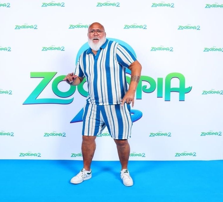 A picture of david fane at the zootopia 2 premiere hitting a pose, wearing a blue and white stripped shirt and shorts combo with white sneakers