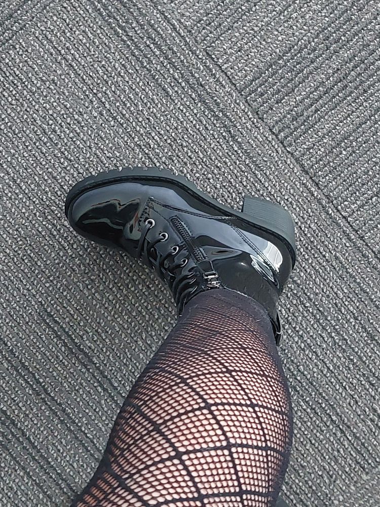 A picture of a leg covered in fishnets and a black shiny boot with a small heel