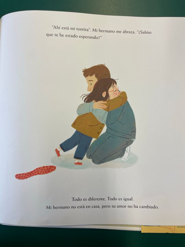 Illustration of the brother and sister embracing. The text at the bottom says: Todo es diferente. Todo es igual. Mi hermano no está en casa pero su amor no ha cambiado./ Everything is different. Everything is the same. My brother’s not at home but his love has not changed. 