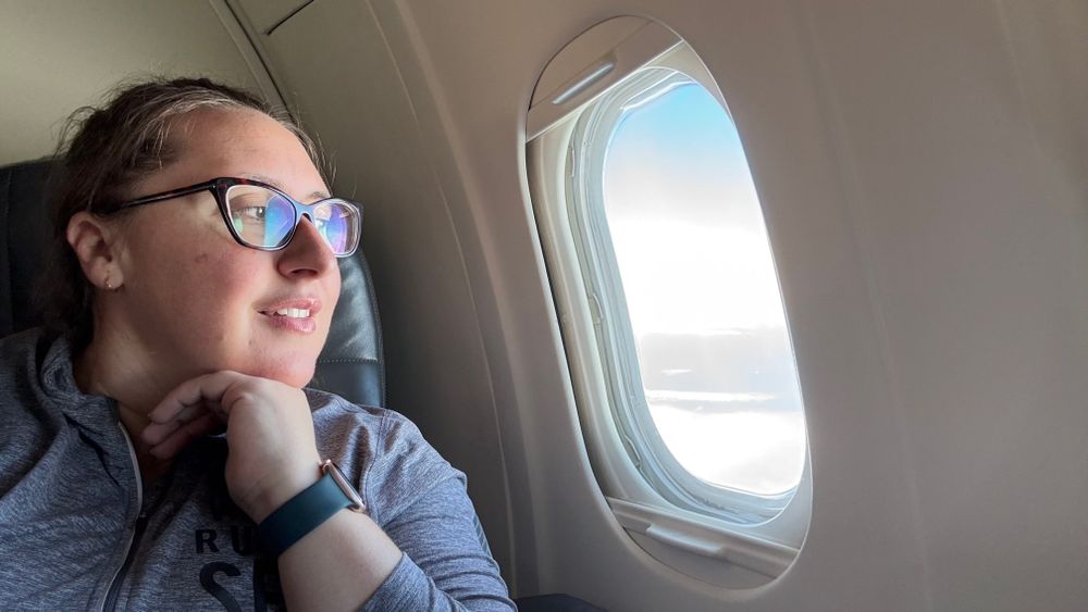 Courtney looks out a window in the last row of an airplane