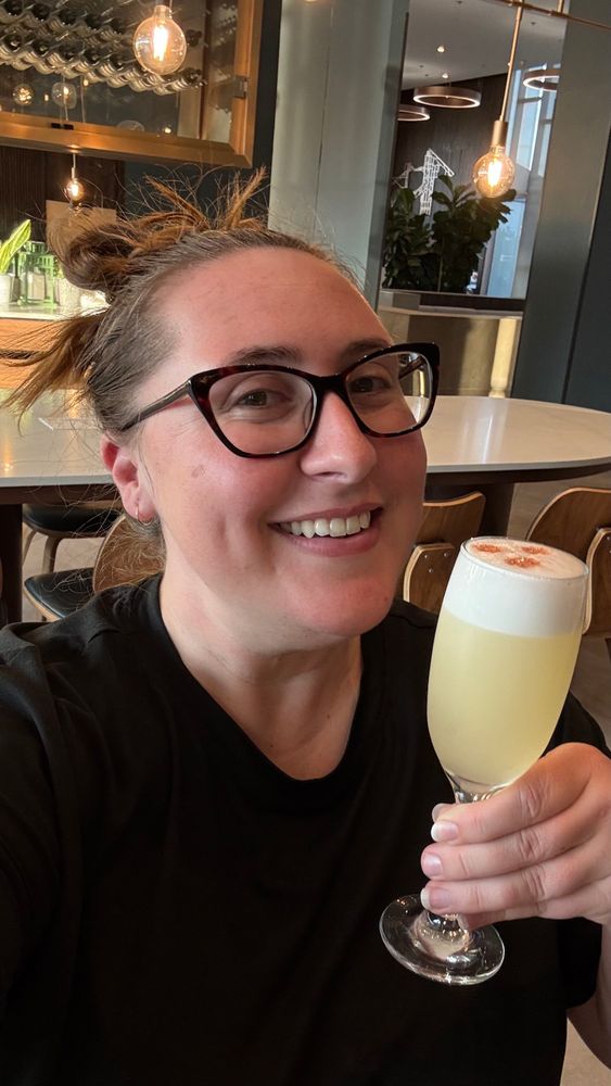 Courtney smiles with a Pisco Sour in a champagne flute. It is delicious with fresh lemon juice and three drops of bitters perfectly placed on the top. 