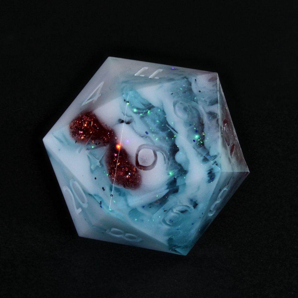 The image is a lone 20 sided die. It sits on a plain black background. The dice is a mix of white and blue with a red streak inside. The numbers are not painted as the dice were not finished at the time of the picture