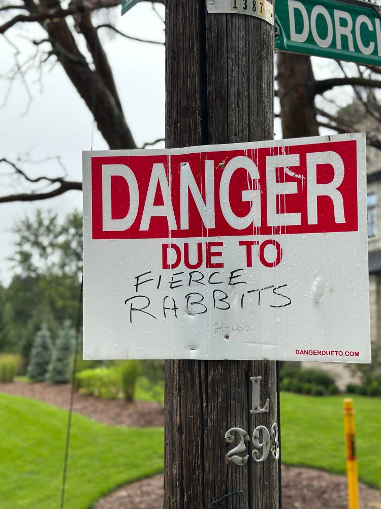 Red and white warning sign tacked to pole: DANGER DUE TO and someone hand wrote “FIERCE RABBITS”