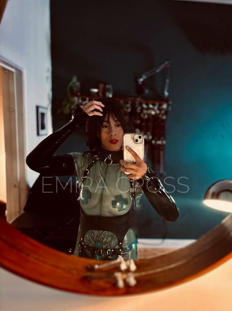 Person is wearing green and black latex and photographs themselves in front of a mirror. 
