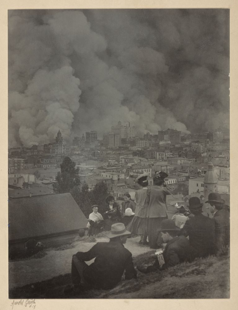 A black and white photograph showing the aftermath of the San Francisco earthquake of 1906. The image shows a group of people sitting on a hilltop watching fires burn the city below.