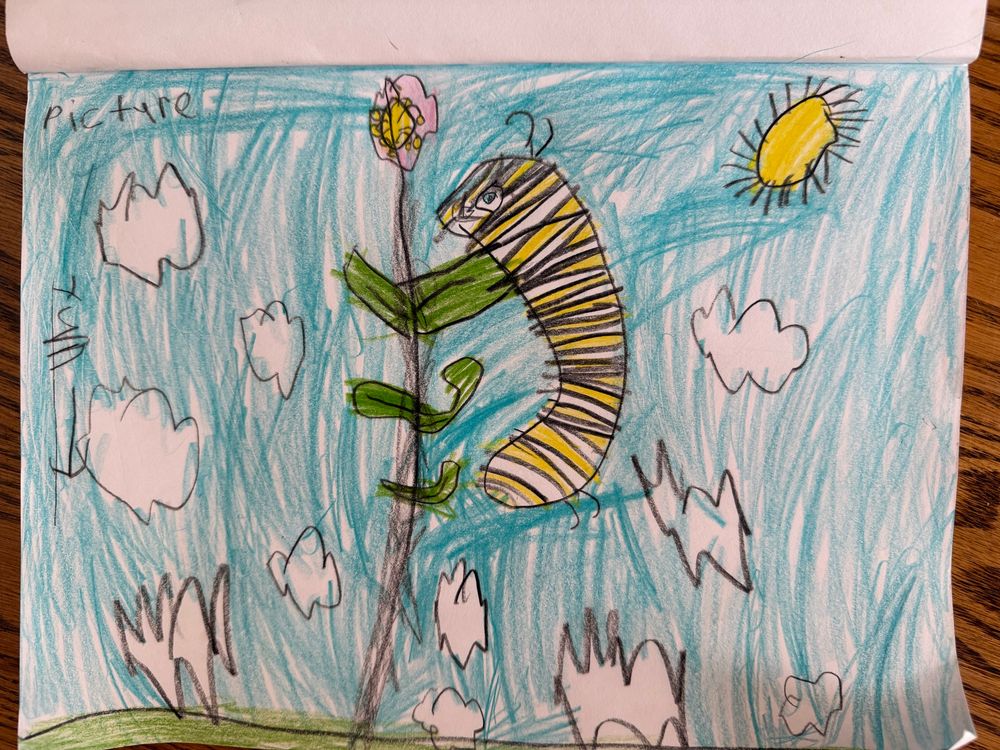 Monarch caterpillar climbing a plant with green leaves and a pink flower with white puffy clouds and blue sky in the background.