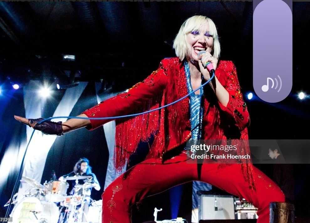 sängerin karen o in einem roten anzug mit troddeln an den armen und viel strass, darunter eine blaue hemdbluse und abgeschnittene lederhandschuhe