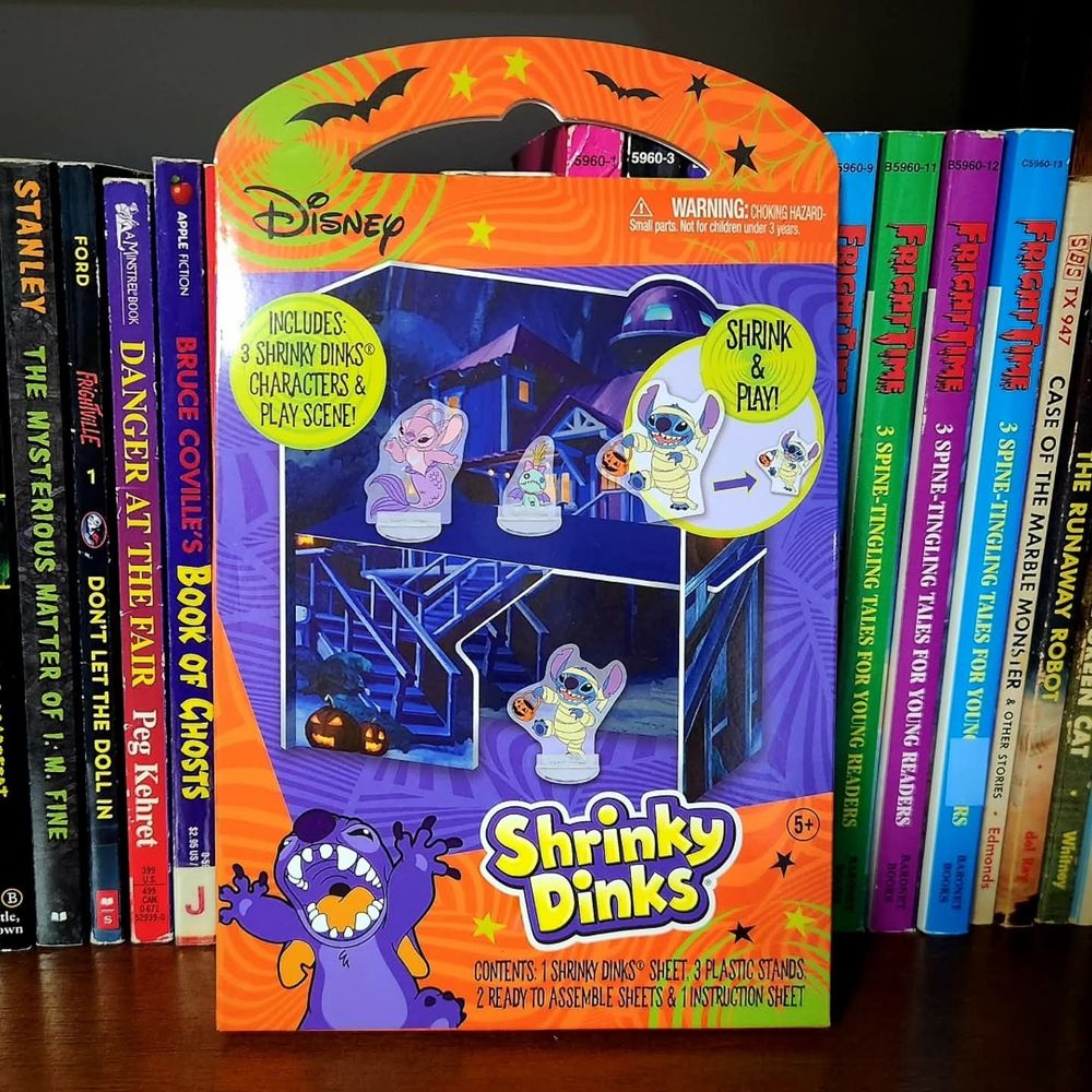 A package of Halloween-themed LILO & STITCH Shrinky Dinks, in front of some books.