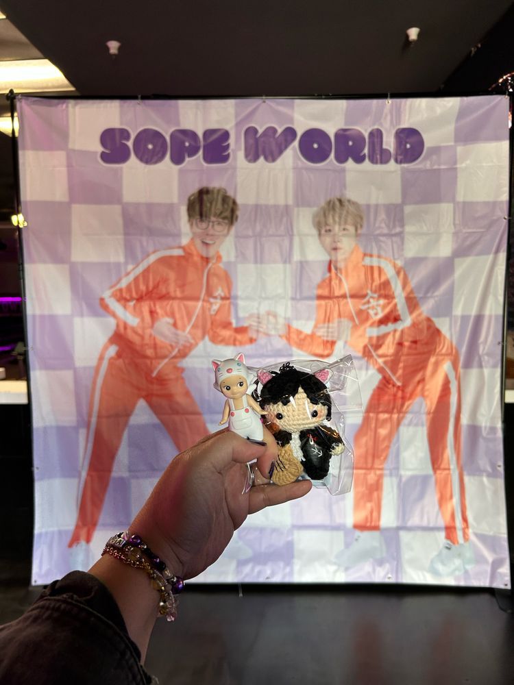 Photo of Sope World banner of Jung Hoseok & Min Yoongi wearing orange jumpsuits while I’m holding a Sonny Angel & crocheted Yoongi amigurumi