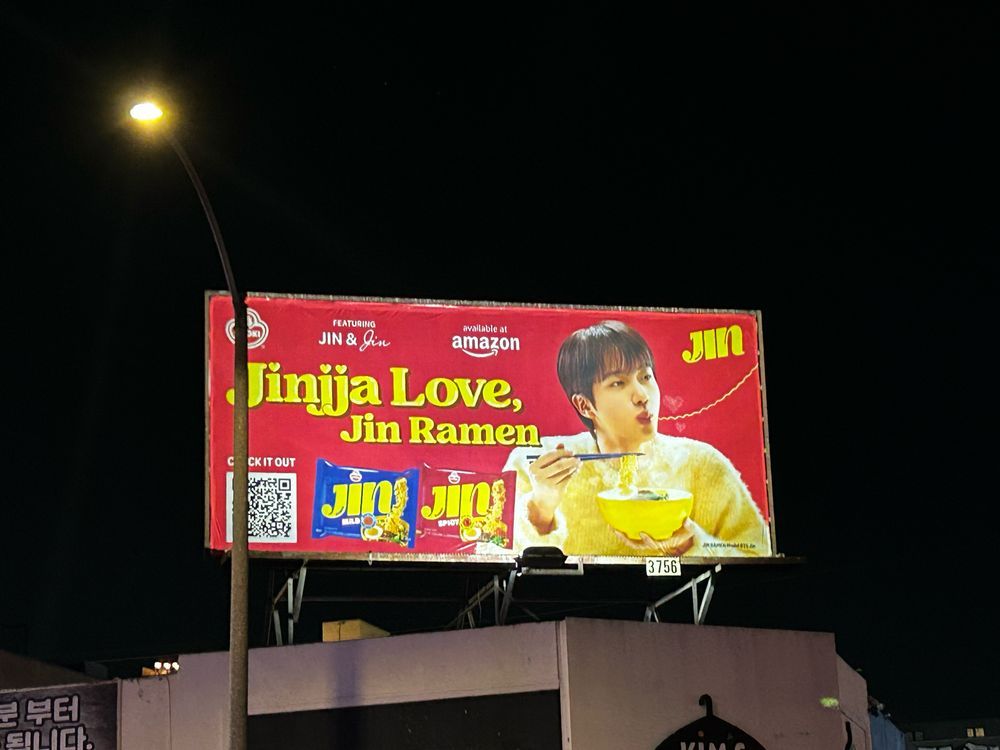 Promotional billboard of BTS JUn earring a bowl of Jin Ramen. 