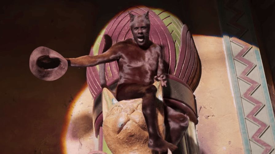 Idris Elba in Cats. Extremely naked, sitting on top of a cat statue while holding his hat.