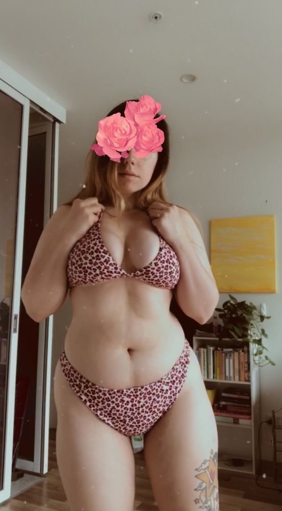 woman standing in a living room, wearing a pink bikini. There are pink roses partially obscuring her face.