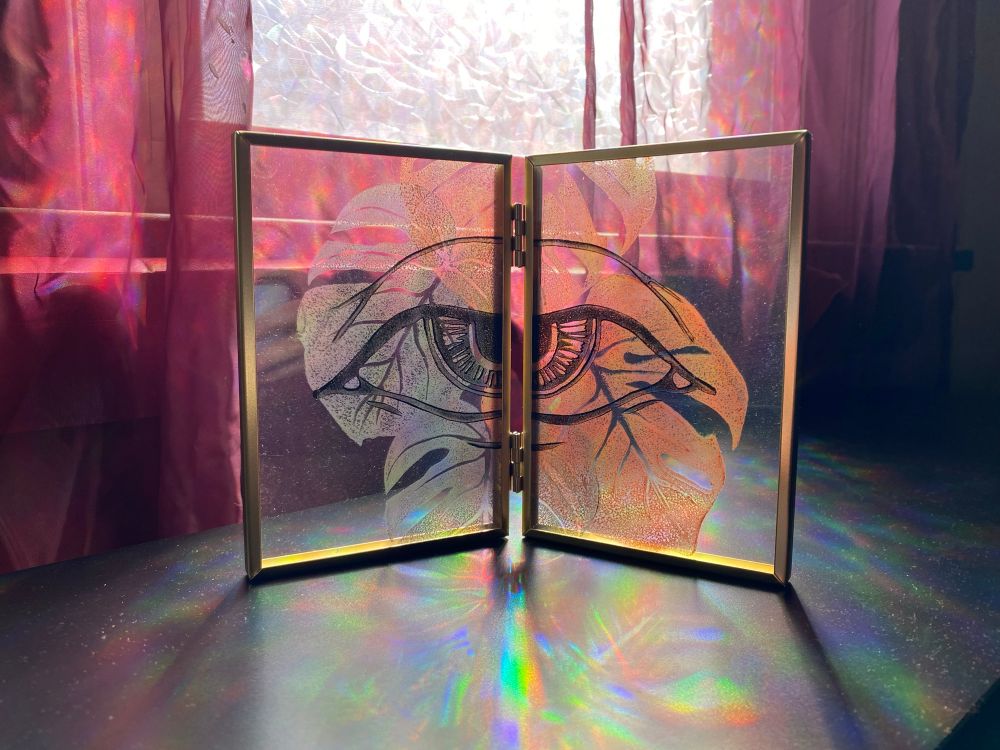 A brass toned frame with metallic monstera leaves and black eye print. 