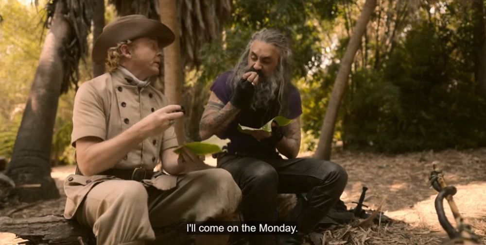 screenshot from s1e7 of hit tv show our flag means death when ed and stede are eating their snake snack. there is closed captioning of stede’s line ‘I’ll come on the monday’ 