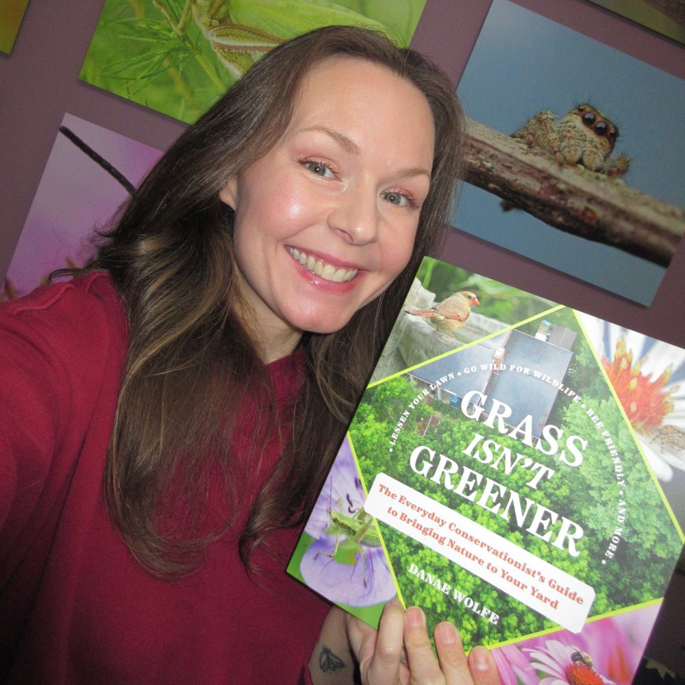 Smiling women with long brown hair holds up book titled “Grass Isn’t Greener.”