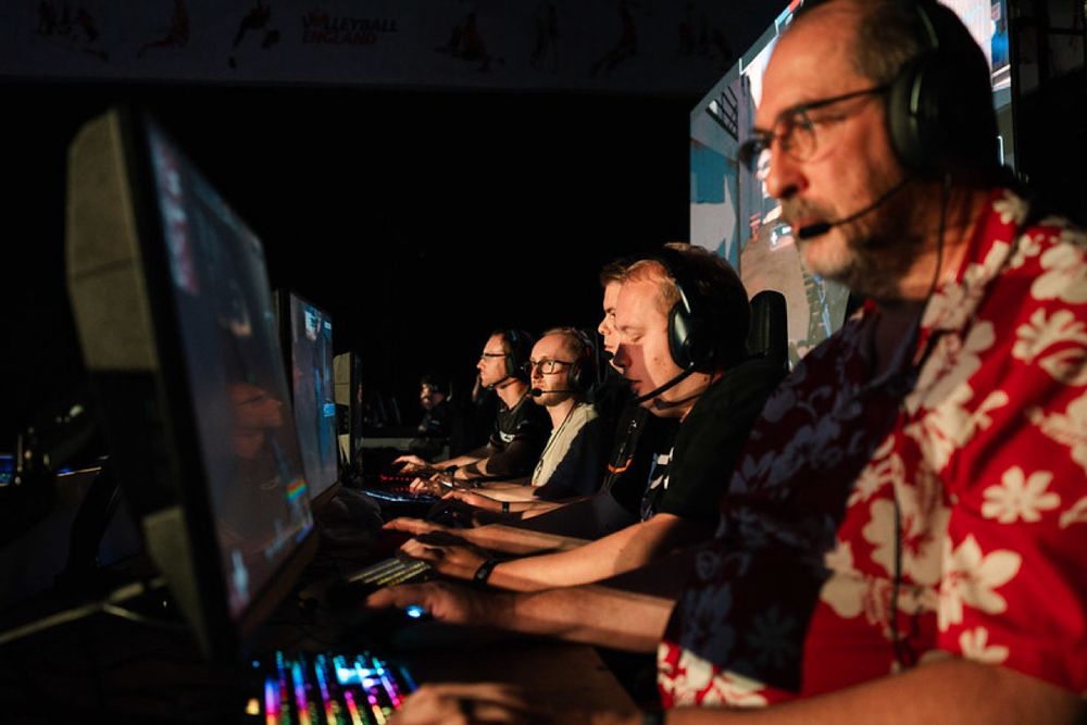 A group of 5 PC gamers on stage at and EPIC.LAN event playing Overwatch 2, with an LED wall behind them. 