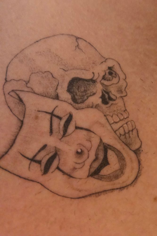 Fineline tattoo of the comedy theater mask with a skull where the tragedy theater mask would normally go. 