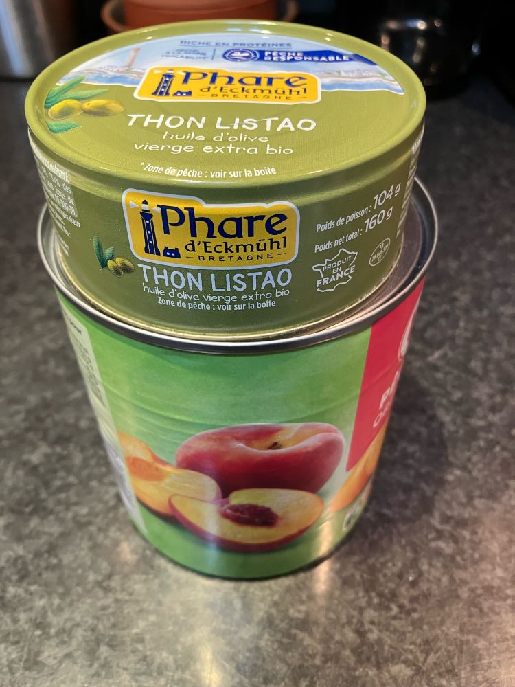 Boîte de 820g de pêches grecques surmontée d’une boîte de thon listao