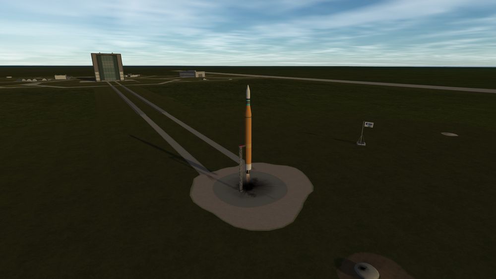 a Mostly orange rocket with an upper stage that has a cyan and green fuel tank. The First stage of the rocket is firing up its engine. Its the day time and there's an ESA flag as the rocket lift offs. You can also see the launch complex from behind including the rocket integration facility/place where I design the rockets in game