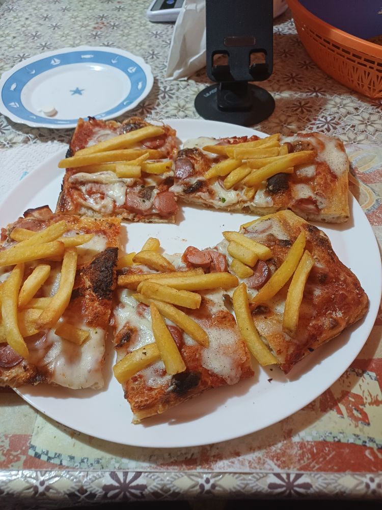 A square shaped pizza with lots of fries and sausages on it. It's on top of a white ceramic plate. Also, there's some vitamin pills on a white and blue plate cause I do need those.
