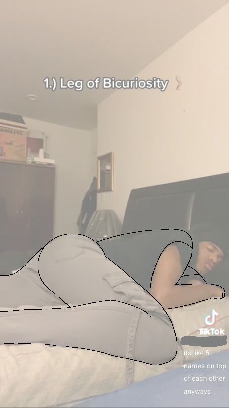 a tiktok screenshot of a man laying on his bed in a specific way, which he called the "leg of bicuriosity". it's sleeping on your side with your knee up at midriff height, arms can be wherever but his are under his pillow.
