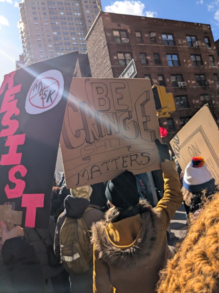 A person holding a sign that says "Be cringe, shit matters"