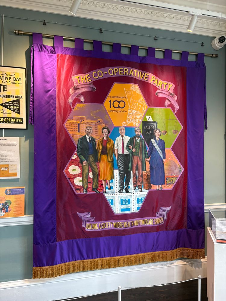 Close up of banner, marking 100 years of the Co-operative Party, with purple border and a group of people including Joyce Butler