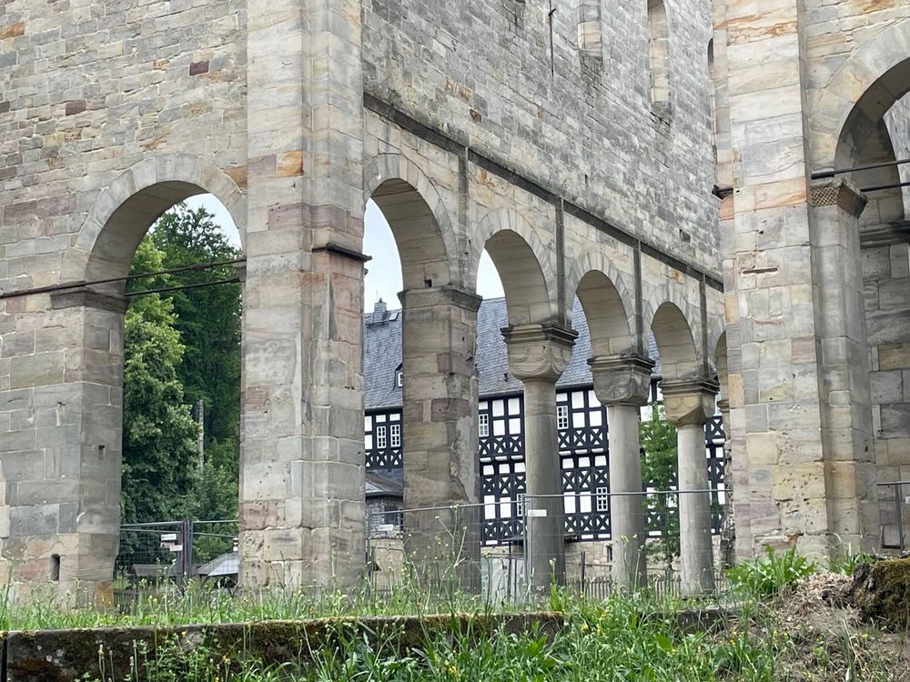 look through the nave's columns to see in the background a half timbered house attached to the medieval building. grass and stone in the ruin.