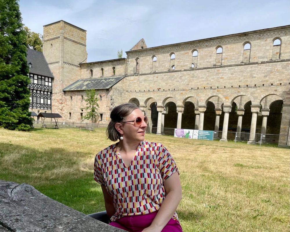 close up shot of me in bright colours and sun glasses sitting in front of the church's massive ruined walls and tower, looking afar.