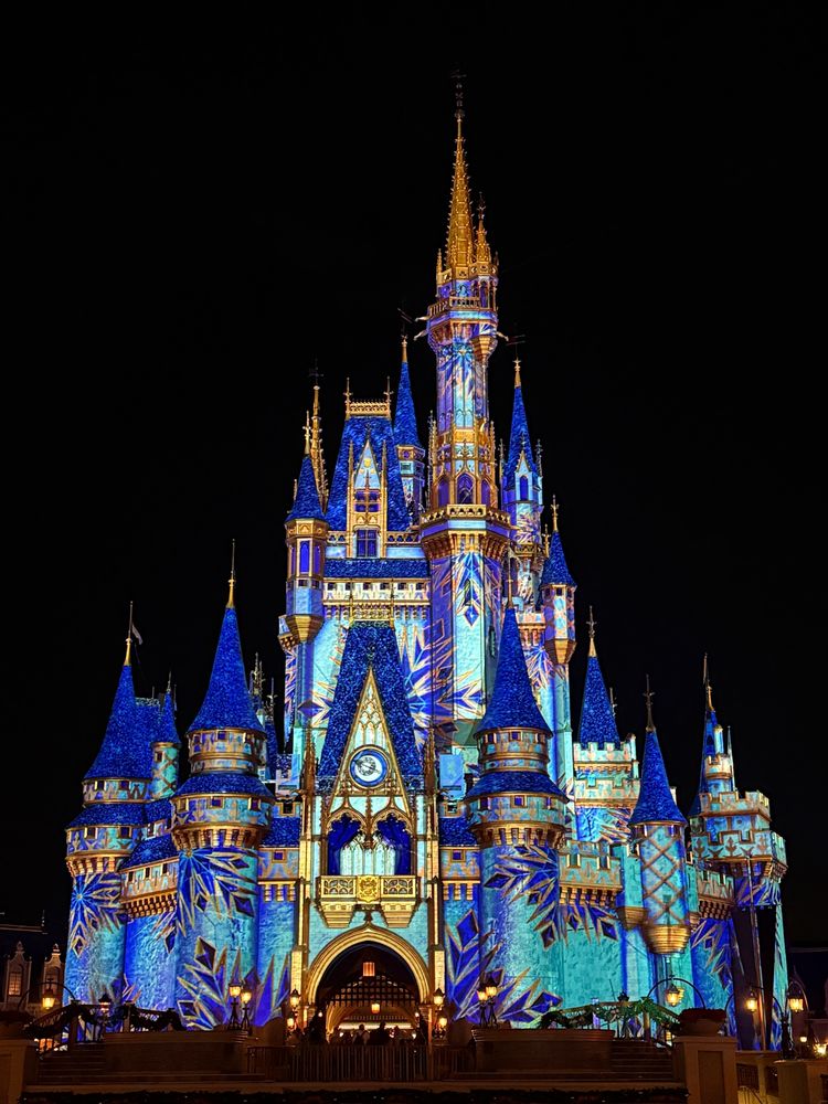 Disney world castle light up for the holiday season at night. Castle towers are blue Andre castle is gold and blue hues. 