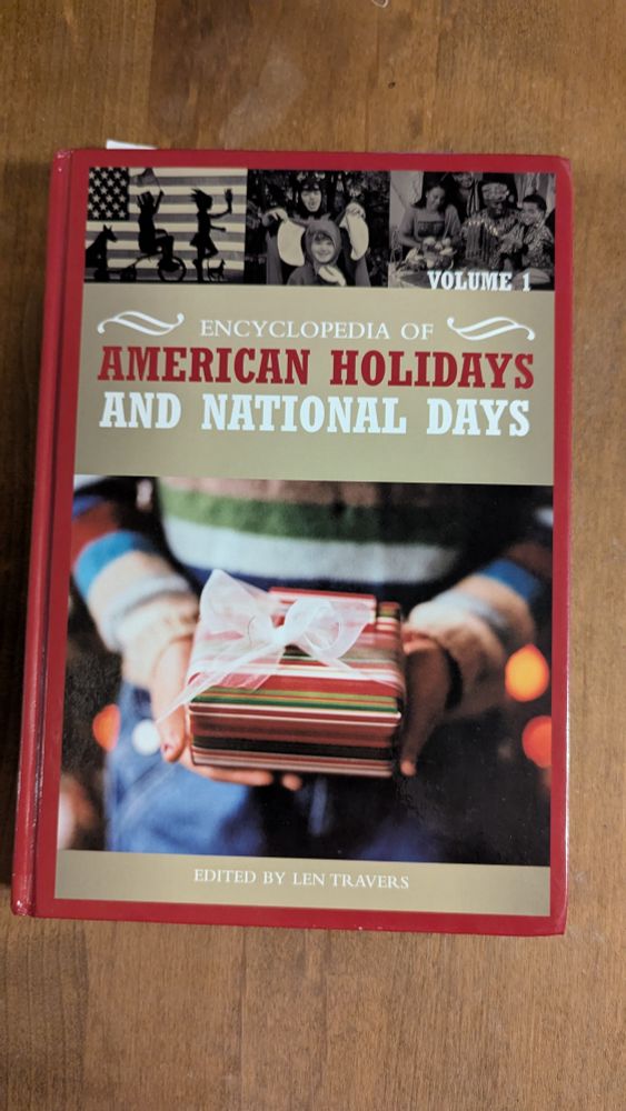 The book cover of "Encyclopedia of American Holidays and National Days," edited by Len Travers. The cover has a photograph of someone holding a wrapped present, with smaller sepia images of children in front of an American flag, children in Halloween costumes, and a family celebrating Kwanzaa.