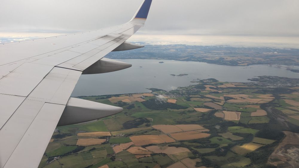 An airplane wing with Scottish land and water below.