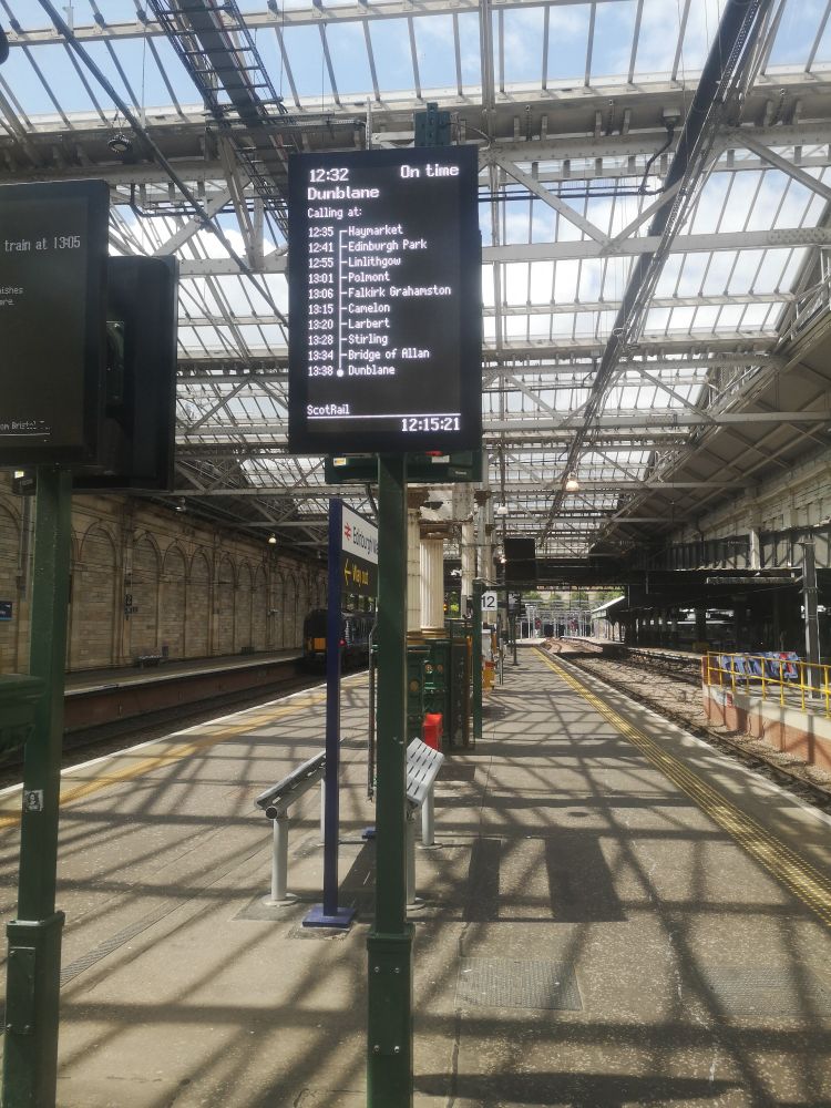 On platform 12 Edinburgh Waverley station with sun streaming in through roof windows. Board announcing train to Dunblane. Stirling is penultimate station.