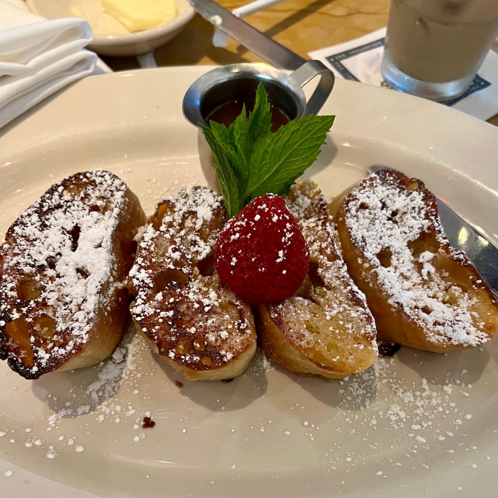 Four slices of French toast from a baguette, dusted with powdered sugar, topped with a strawberry and a sprig of mint. 