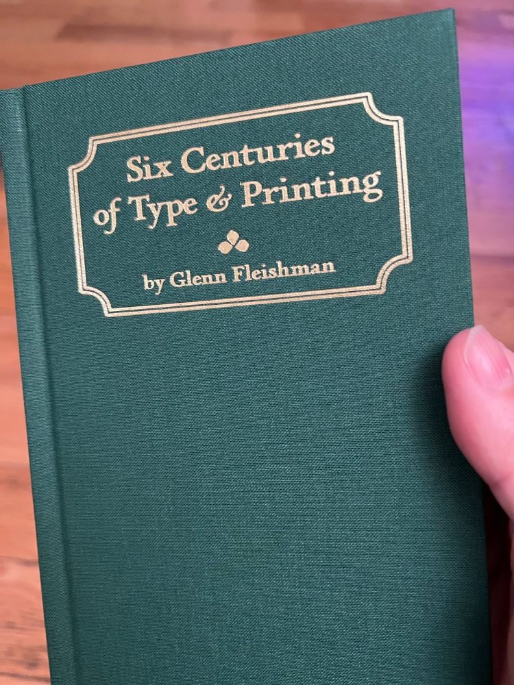 A slender green hardcover book titled “Six Centuries of Type & Printing” by Glenn Fleishman, being held in my right hand. 
