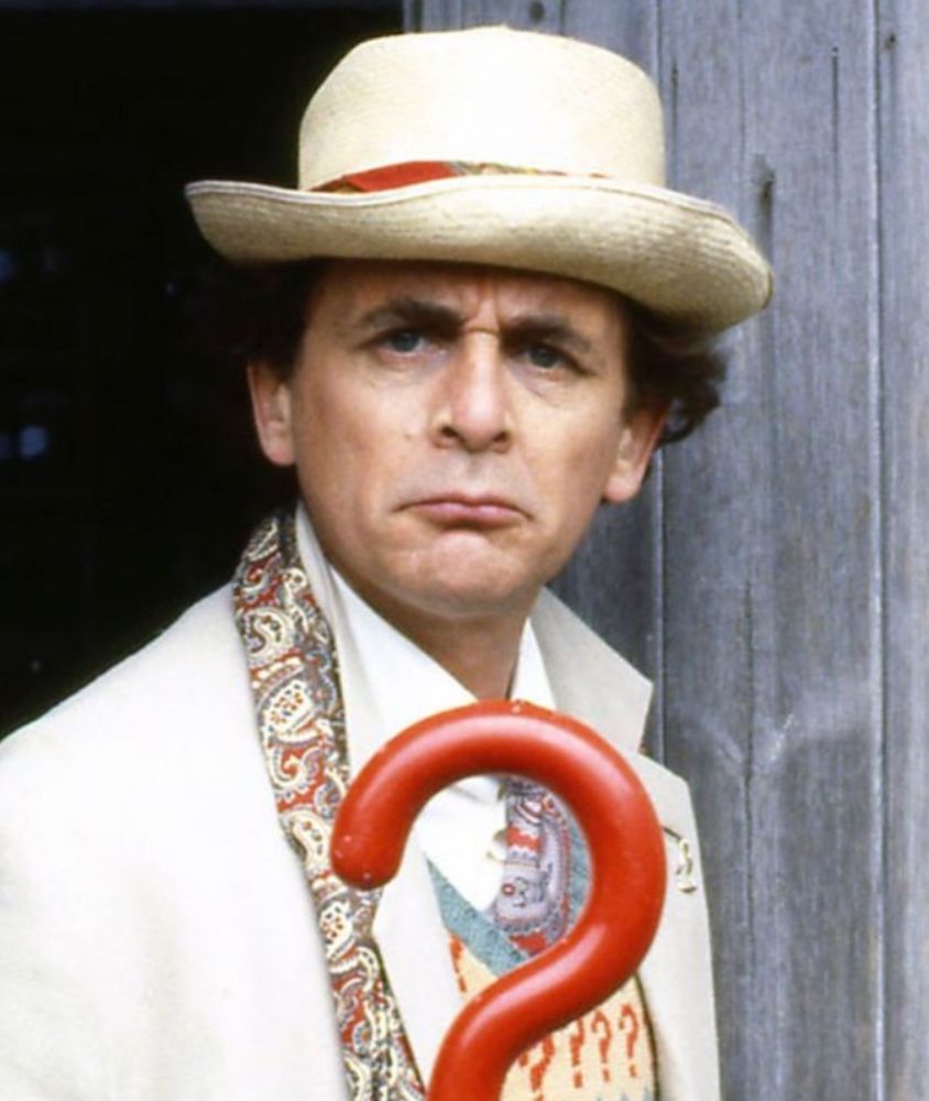 A man with hat and umbrella frowning towards the camera 