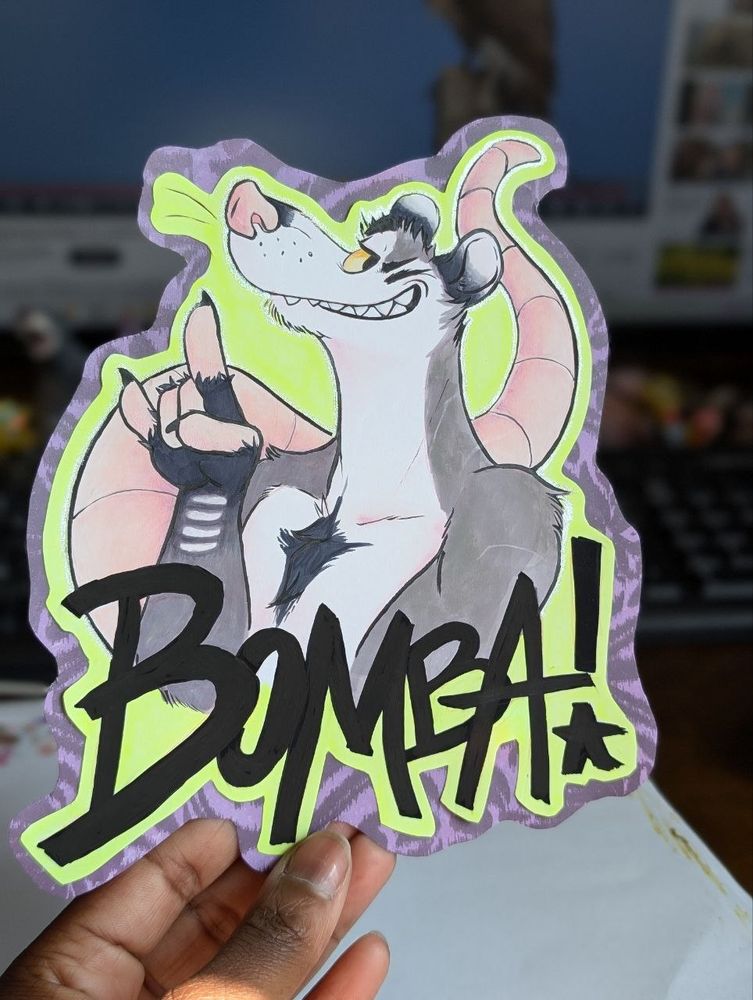 Physical paper art of a cool punk badger named Bomba! throwing up the devil horns hand gesture. The possum is surrounded by a florescent highlighter green while the edges are a dark purple