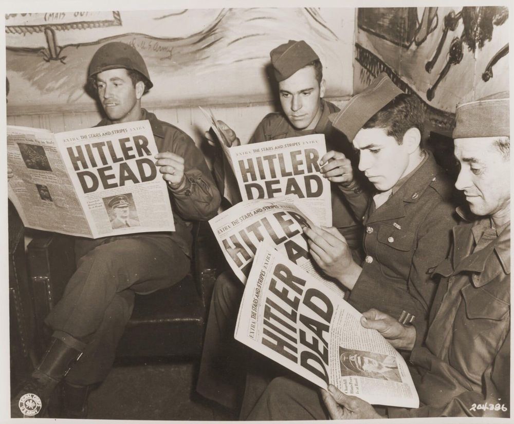 Soldiers reading newspaper announcing Hitler’s death.